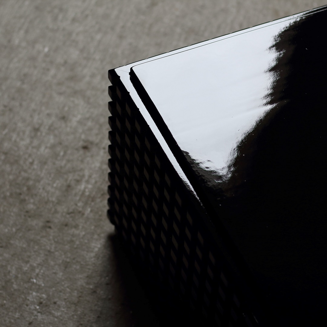 Oblique Noir Een meubel die door het licht een unieke verschijning is, gemaakt van resthout, diepzwart gebeitst en met een glanzende lak afgewerkt. De naam is ontstaan door de vorm van de zijkanten van het frame wat in het Nederlands letterlijk vertaald schuin zwart betekent.