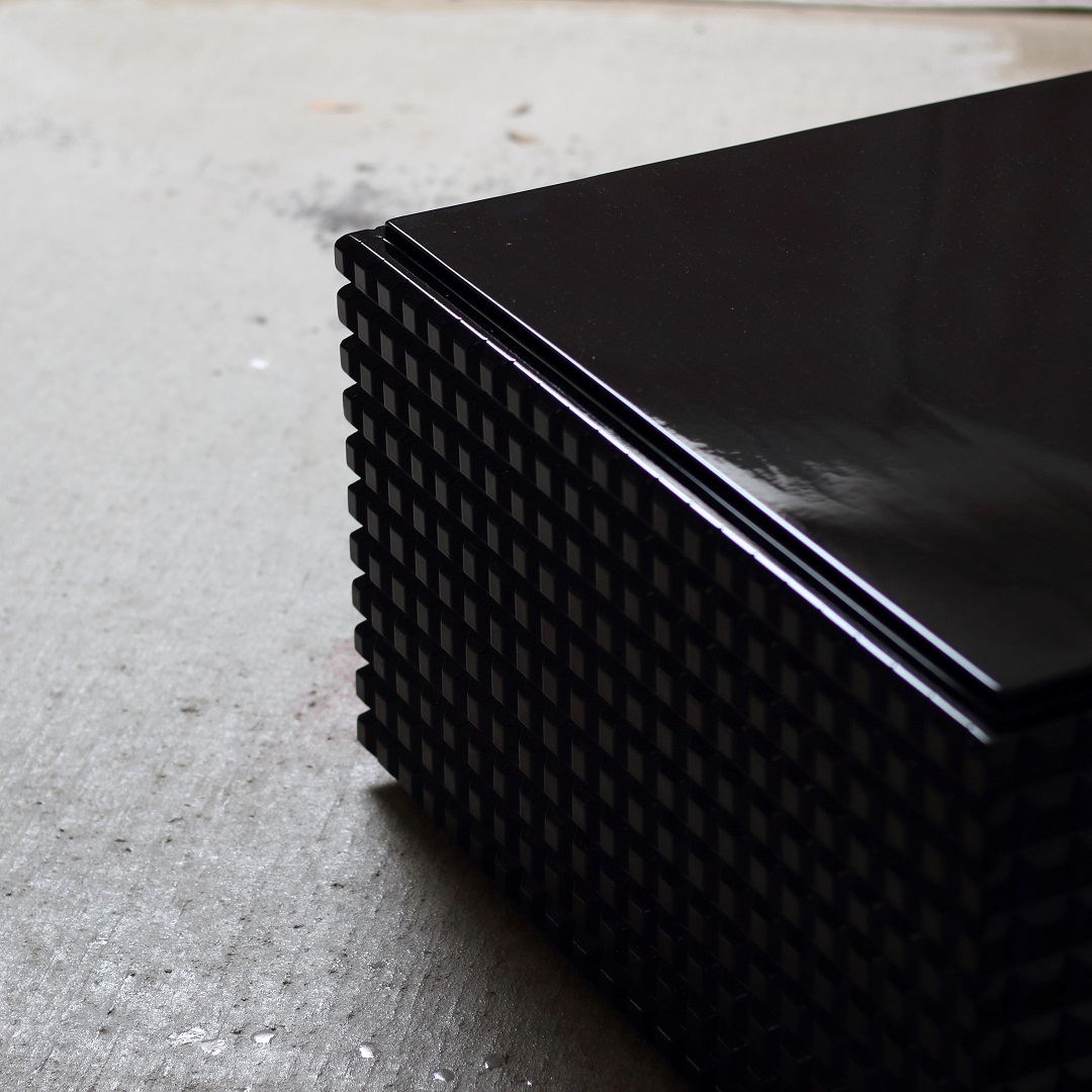 Oblique Noir Een meubel die door het licht een unieke verschijning is, gemaakt van resthout, diepzwart gebeitst en met een glanzende lak afgewerkt. De naam is ontstaan door de vorm van de zijkanten van het frame wat in het Nederlands letterlijk vertaald schuin zwart betekent.